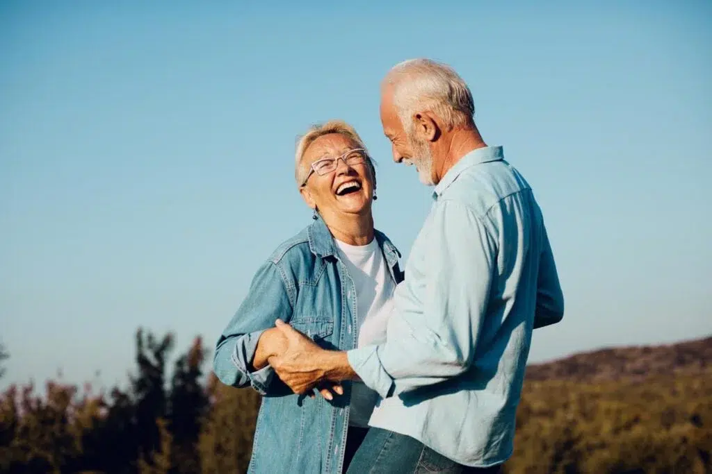 Older couple walking outdoors with a dog, smiling.